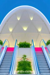 View of two escalators with greenery in a modern architectural setting, illuminated by warm lighting.