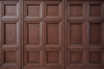 Full frame texture of classic dark brown wooden wall paneling with square molding pattern.