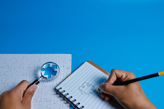 Problem solving concept. A hand sketches the puzzle piece while another hand holds a magnifying glass highlighting a missing piece representing identifying missing information and finding solutions.