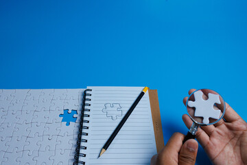 Problem solving concept. white puzzle with a missing piece and a sketched puzzle in a notebook while a hand holding a piece under a magnifying glass, symbolizing analysis and problem solving.
