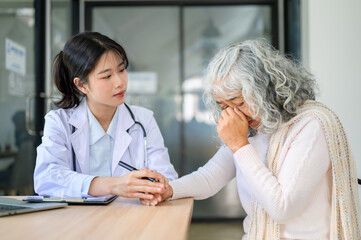 Obraz premium Asian woman doctor holding hand comforting a crying old patient sitting at table in diagnosis room