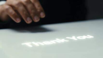Close up of business person's hand interacting with glowing 'Thank You' text on a modern table for digital gratitude concept and innovative communication