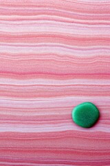 A smooth green stone rests on a textured pink sandstone background, creating a contrast of color and texture.