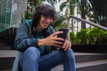 Young man smiling happily sitting on the stairs while using a smartphone