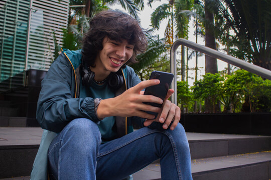 Young man smiling happily sitting on the stairs while using a smartphone