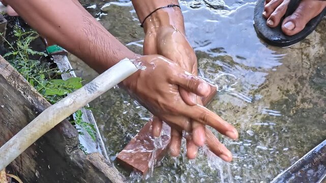 Footage of a man washing his hands under a small pipe with flowing water in a simple outdoor setting. A natural, rustic hygiene moment showing clean, minimal, and traditional living.