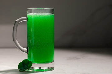 Bright Green Beer In Glass Mug, Frothy Foam And Fine Bubbles Rising, Small Clover Resting At Base On Marble Surface, Moody Studio Lighting Casting Vivid Emerald