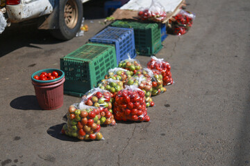Fresh red and green tomato in bag for sale at rustic outdoor market. This agriculture produce, healthy vegetable, sits on street next to crate and vehicle