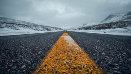 Empty road with yellow line through snowy mountains, cloudy sky