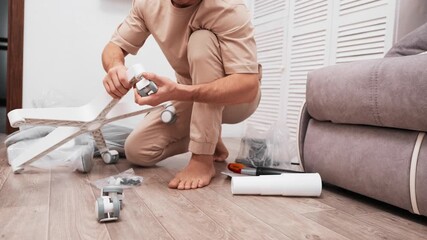 Man carefully attaches wheels to base computer chair, in bright interior with soft sunlight. Practical skills for working at home, attention to detail, and calm rhythm of chair assembly.