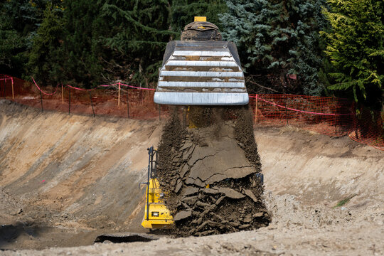 Closeup of large excavator bucket dumping out a load of dirt while digging a large foundation pit for a stormwater retention system, earthworks construction project site