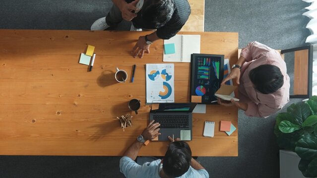 Top view of skilled project manager talking about financial graph to investors while sitting at meeting table with data analysis document. Diverse team discussing and brainstorming idea. Convocation.