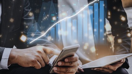 Two business professionals engage with digital tools while analyzing financial data. A graphical representation of market growth enhances their strategic discussion in a modern office. Copula