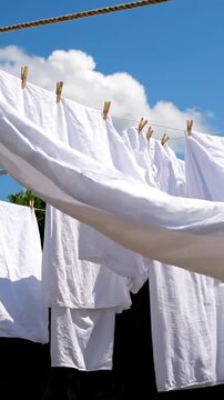 Clean white laundry drying on a clothesline against a bright blue sky with clouds