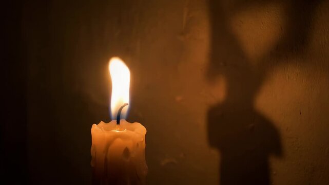 Close-up of a single lit candle flickering gently with a soft warm glow casting a subtle shadow on a textured wall creating a peaceful and atmospheric ambiance for meditation or a quiet evening