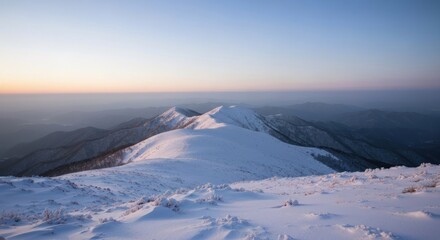 Winter mountain vista at dawn. Snow-covered peaks and ridges extend into a hazy, pale-blue sky