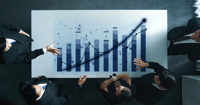 A group of business professionals collaborates to analyze financial data displayed on graphs and charts in a modern office setting. Insightful teamwork enhances strategic planning. Axiom