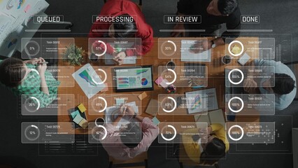 A top-down view of a collaborative team in an office setting, discussing project management with visible progress tracking and data visualization on the table. Raster