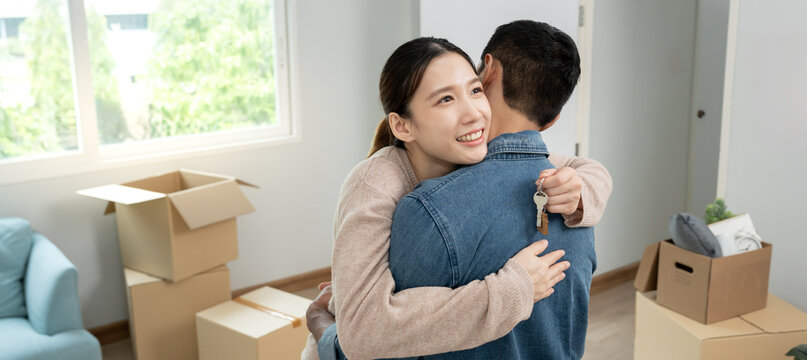 Moving house, relocation. Wife hug husband and show key new condominium or home, inside the room was a cardboard box containing personal belongings and furniture. move in the apartment - Powered by Adobe