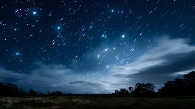 Vast starry night sky with luminous star trails captured in long exposure over a serene rural landscape and clouds