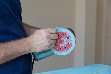 Man taking sanding disk off of orbital sander
