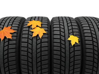 Set of four new winter tires with fallen autumn leaves scattered on their treads, symbolizing seasonal change and vehicle preparation for cold weather.