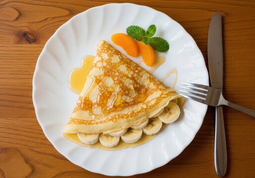 Delicious folded crepe filled with fresh banana slices and topped with orange segments and mint leaf