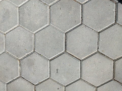 A detailed, top-down view of a textured grey hexagonal paving stone surface. The pattern creates a geometric and uniform background, suitable for construction or design