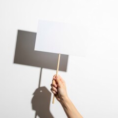 Hand holds a blank sign on a stick, casting shadow on white background