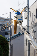 高所作業車に乗って住宅街の電線を修理する作業員