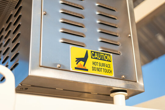 Hot surface safety caution sign label on the electrical junction box, information to identify hazard in workplace. Industrial working sign, close-up and selective focus.