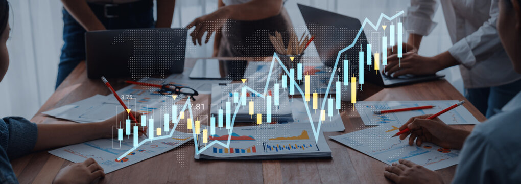 Business team collaborates on stock market analysis during a meeting, using charts and electronic devices on a wooden table to strategize investments and financial growth. Gantry