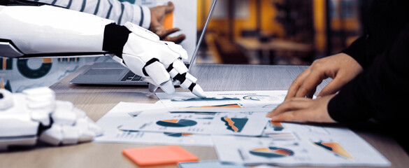 A human hand collaborates with a robotic arm as they analyze data in a modern workspace, illustrating the synergy of technology and human expertise in decision-making.Noogenesis