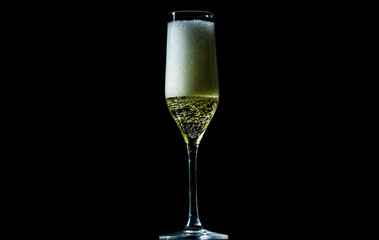 Champagne sparkling in a crystal glass. Pouring bubbly champagne with festive bubbles. Close-up of sparkling wine splash in elegant wineglass. Champagne drink with golden fizz on black background.