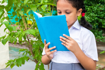 Asian Indian school girl in uniform reading book with blue plain and empty cover. copy space at book for any text