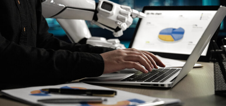 A modern workspace showcasing a human interacting with a laptop while a robot assistant displays data analytics, emphasizing the fusion of technology and business processes.Noogenesis - Powered by Adobe