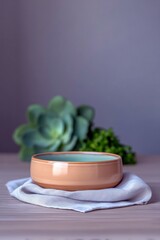 A ceramic bowl rests on a linen napkin, with a succulent plant and green foliage in the background. The scene is lit with soft, natural light.