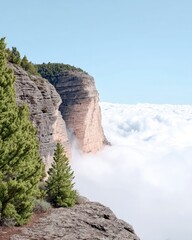 Scenic landscape featuring a cliff, clouds, trees, and blue sky. The image captures a natural environment with a bright, airy atmosphere.