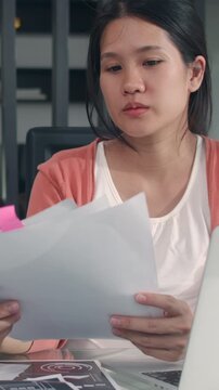 Vertical Screen : Young Asian Pregnant woman use laptop records of income expenses at home. Dad giving milk wife record budget, tax, financial document working in living room at house in morning.