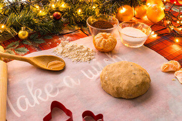 Homemade Christmas cookie preparation with dough, flour, cookie cutters and festive decorations on a kitchen table. Holiday baking process with ingredients and gingerbread shapes.