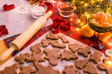 Unbaked Christmas cookies in festive shapes arranged on parchment paper. Holiday baking process with gingerbread dough, cookie cutters and warm seasonal kitchen atmosphere.