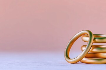 A stack of golden rings on a white surface with a pink background. The rings are arranged in a stack, with one ring leaning against the stack.
