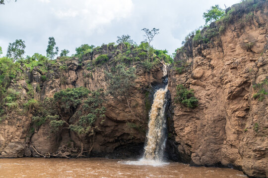 Malika Falls in Nakuru National Park, Kenya, is a stunning waterfall cascading down rocky cliffs surrounded by lush greenery. The water flows into a small pool below, creating mist and a soothing
