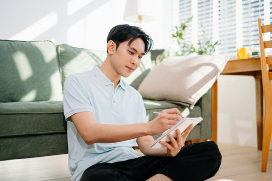 Young asian man relax on comfortable couch at home texting messaging on smartphone and tablet smiling man use cellphone  shopping online from home
