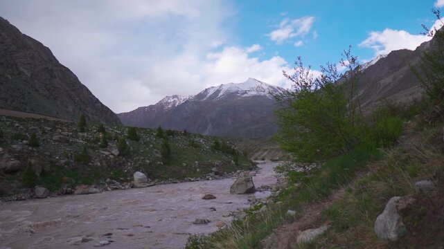 Scenic Landscape shot of Miyar river flowing in front of snowy Himalayan mountain peak with clouds above it during sunset at Miyar Valley in Lahaul and Spiti district, Himachal Pradesh, India.