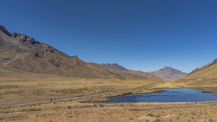 Beautiful high-altitude landscape. Blue lake on the plateau. The railroad tracks run through the valley. Yellow dry grass on the ground. Mountains against a clear azure sky. Copy space. Peru.