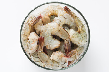 Top view of fresh, raw shrimp, peeled and deveined with tails intact in a clear glass bowl. Ready for cooking, perfect for a stir-fry, grill, or seafood boil.