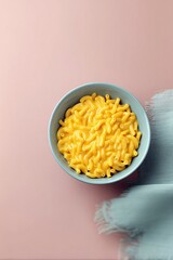 Overhead shot of a bowl of macaroni and cheese on a pink surface with a blue cloth.