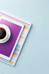 Overhead shot of a tablet with a purple screen, a cup of coffee, and a notebook on a light blue background. Minimalist composition.