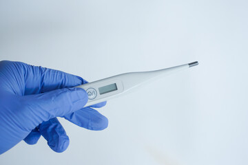 Blue gloved hand holds digital thermometer, clinical background